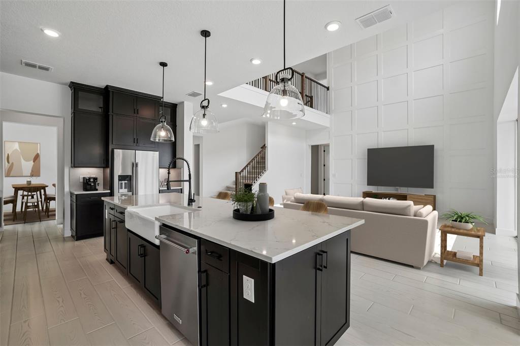 A modern kitchen with dark cabinets and a white island overlooks a living room area — 34931 BLAINE PASS, ZEPHYRHILLS, FL