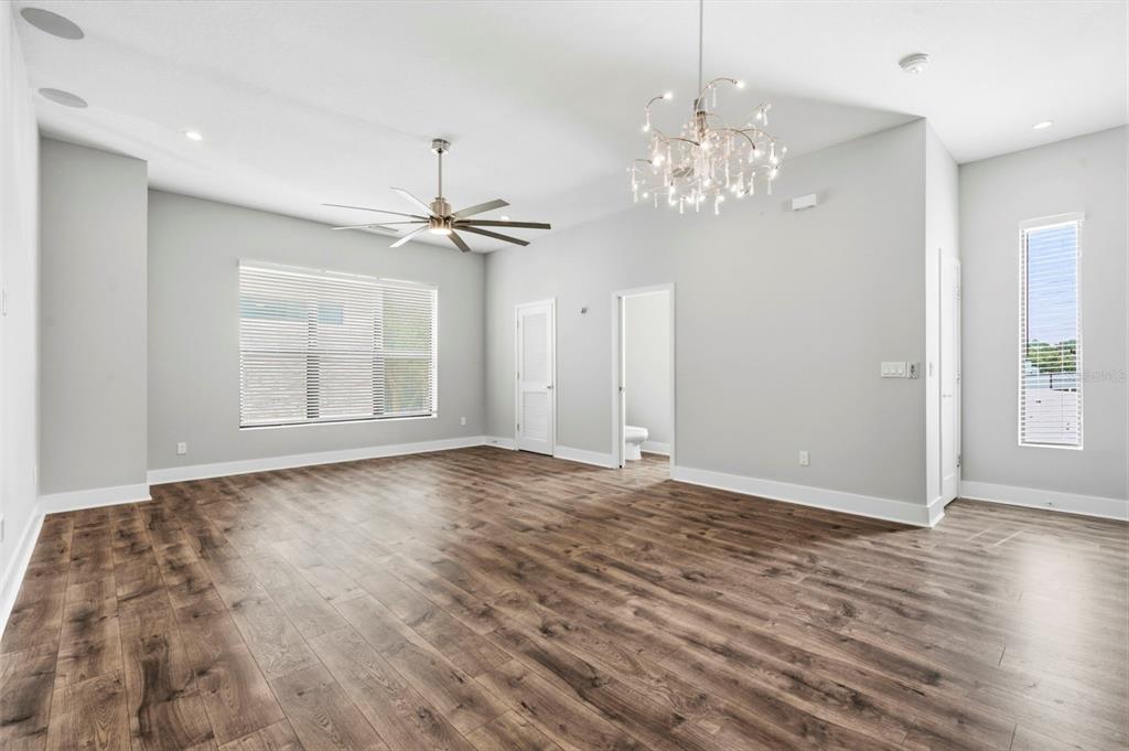 An empty room with light gray walls, wood-look flooring, a ceiling fan, and a chandelier — 4810 W MCELROY AVENUE UNIT 7, TAMPA, FL