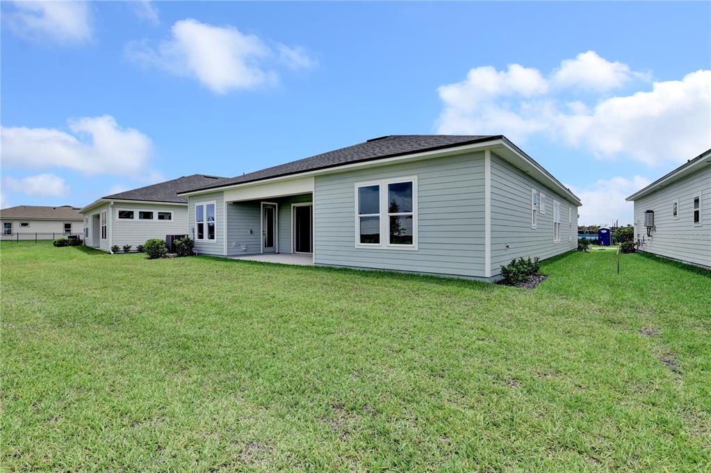 The rear exterior of a light blue single-story house with a covered patio and lawn — 587 KNOTTED BIRCH AVENUE, ST AUGUSTINE, FL