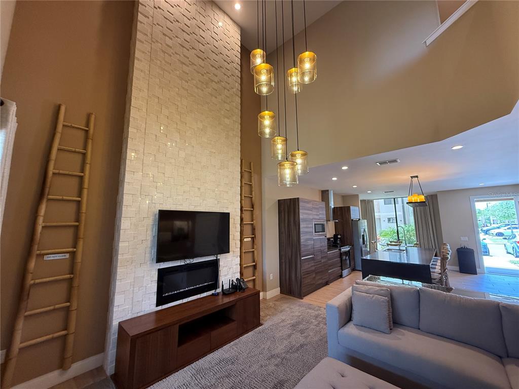 A living room features a tall stone fireplace, a modern chandelier, and an open kitchen — 3065 ROCKEFELLER WAY, KISSIMMEE, FL