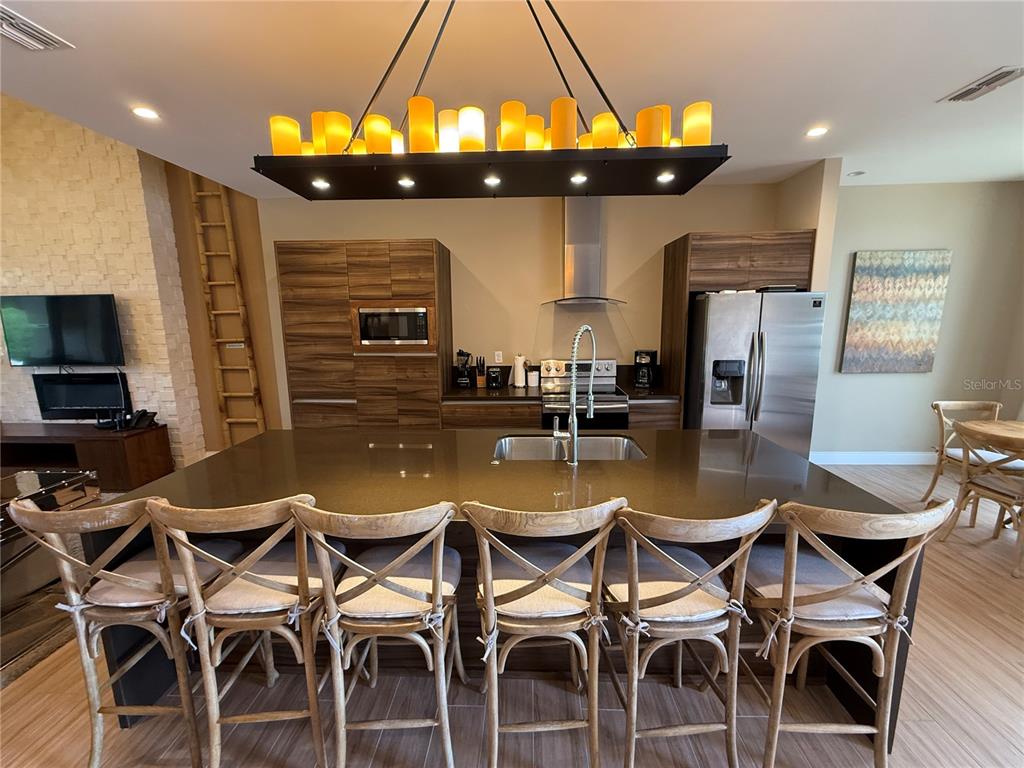 A modern kitchen features a large island with six wooden chairs and a candle-style chandelier — 3065 ROCKEFELLER WAY, KISSIMMEE, FL