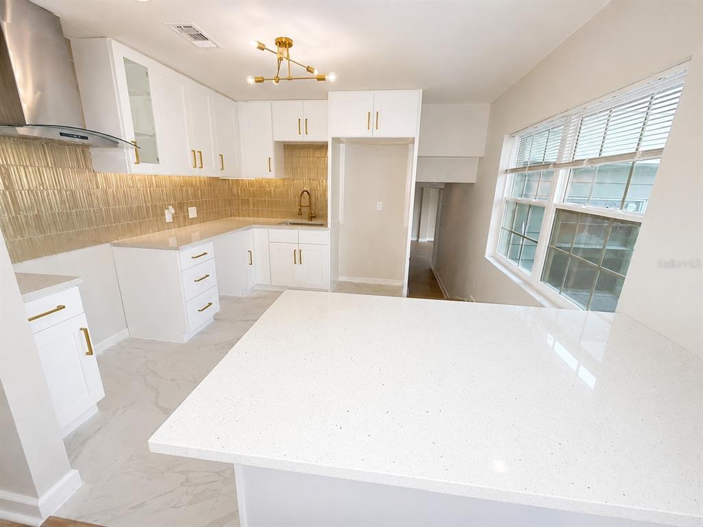 A modern kitchen features white cabinets, quartz countertops, gold hardware, and a gold-tiled backsplash — 118 2ND STREET NW, RUSKIN, FL