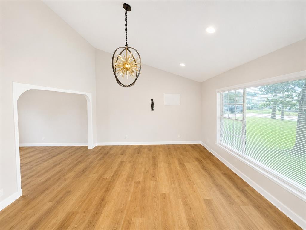 A bright, empty room features light wood-look flooring, a vaulted ceiling, and a modern sputnik chandelier — 118 2ND STREET NW, RUSKIN, FL