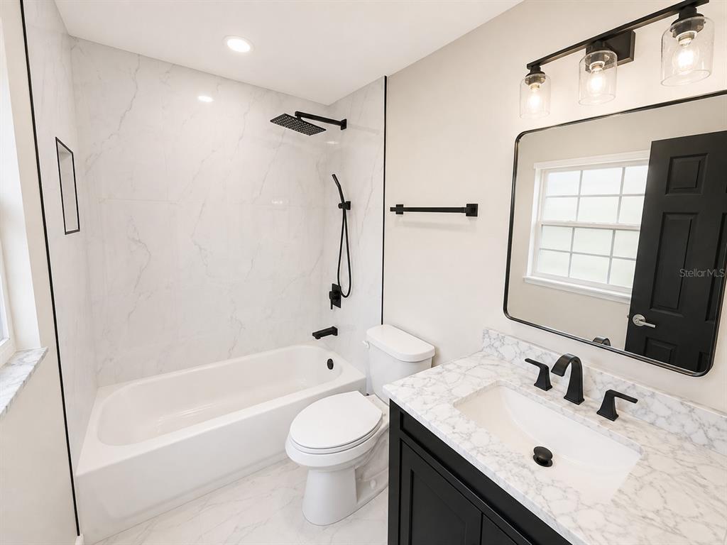 A modern bathroom features a marble-tiled shower, a white toilet, and a black vanity — 118 2ND STREET NW, RUSKIN, FL