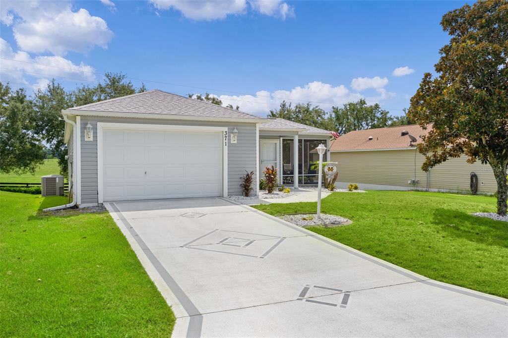 A single-story house with gray siding, a white garage door, and a decorative concrete driveway — 371 ARBELLA LOOP, THE VILLAGES, FL