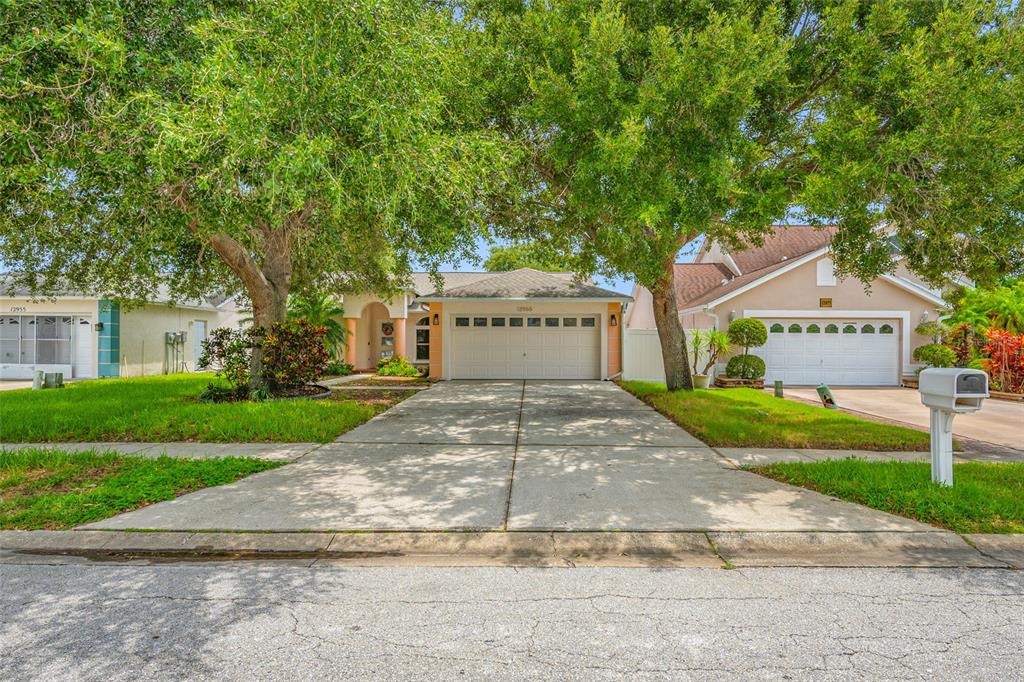 A single-story house with a two-car garage, concrete driveway, and large trees in the front yard — 12965 PINEFOREST WAY W, LARGO, FL