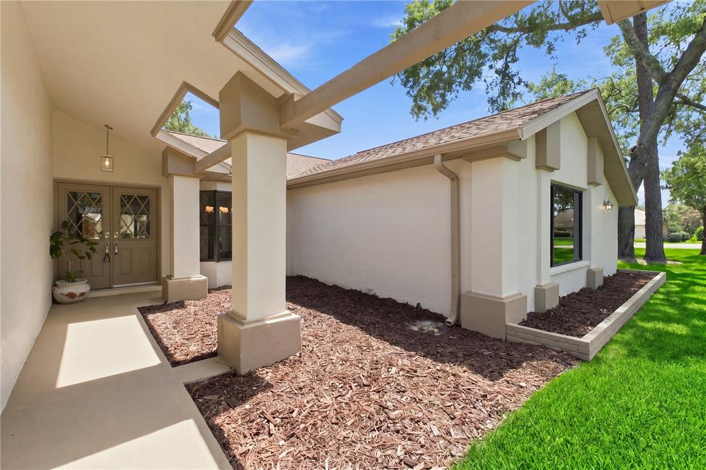 A beige house exterior features a covered entryway with square columns and a mulch bed — 9429 COBBLER COURT, WEEKI WACHEE, FL
