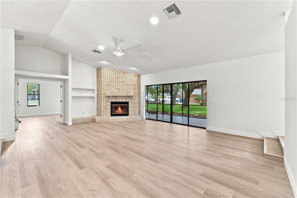 A living room with light wood floors, a brick fireplace, and large sliding glass doors — 9429 COBBLER COURT, WEEKI WACHEE, FL