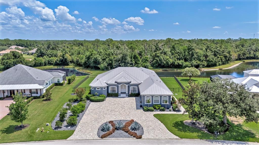 An aerial view shows a gray house with a metal roof and paved driveway — 1911 148TH COURT E, BRADENTON, FL