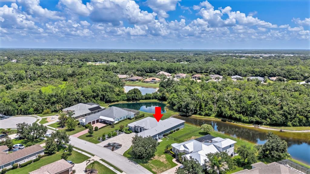 An aerial view shows a suburban house with a red arrow pointing to its roof — 1911 148TH COURT E, BRADENTON, FL