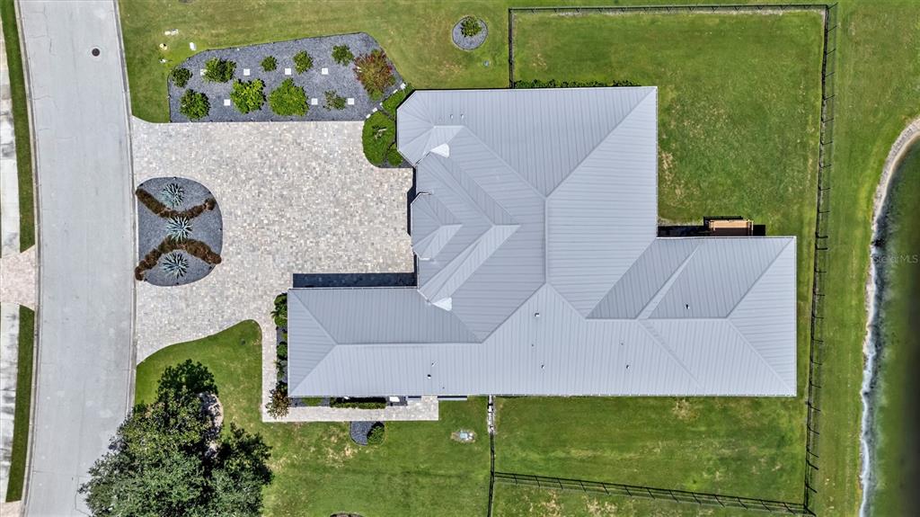 An aerial view shows a house with a metal roof, a paved driveway, and landscaping — 1911 148TH COURT E, BRADENTON, FL