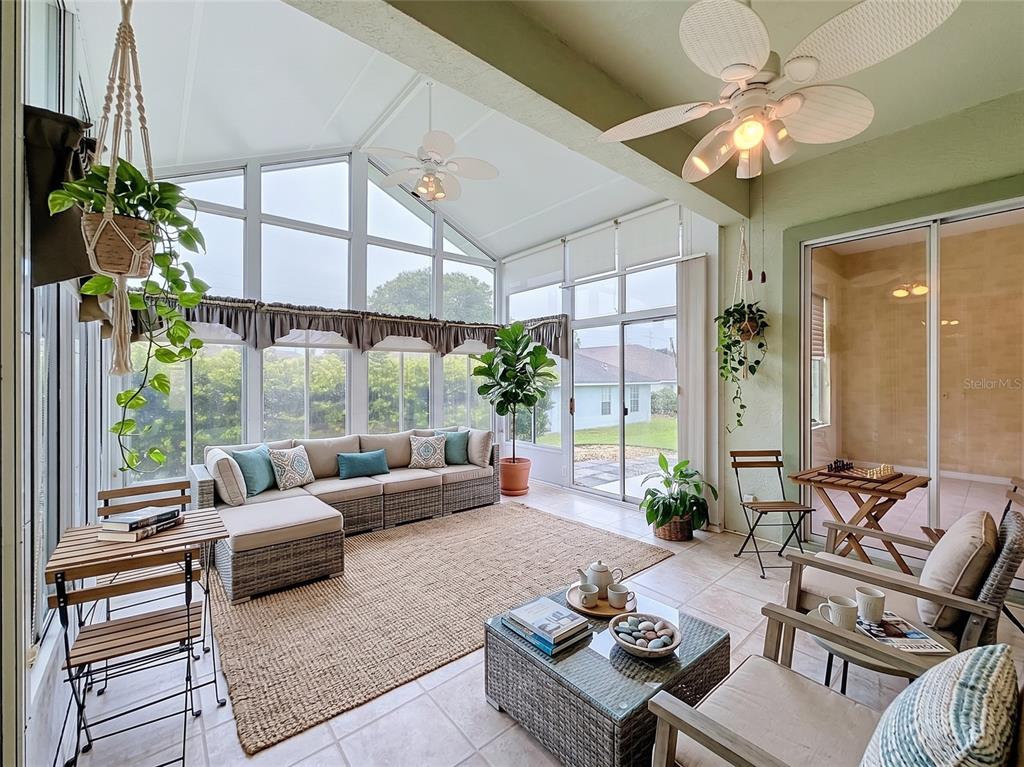 A sunroom features a sectional sofa, a glass-top coffee table, and large windows overlooking grass — 11932 SE 179TH STREET, SUMMERFIELD, FL