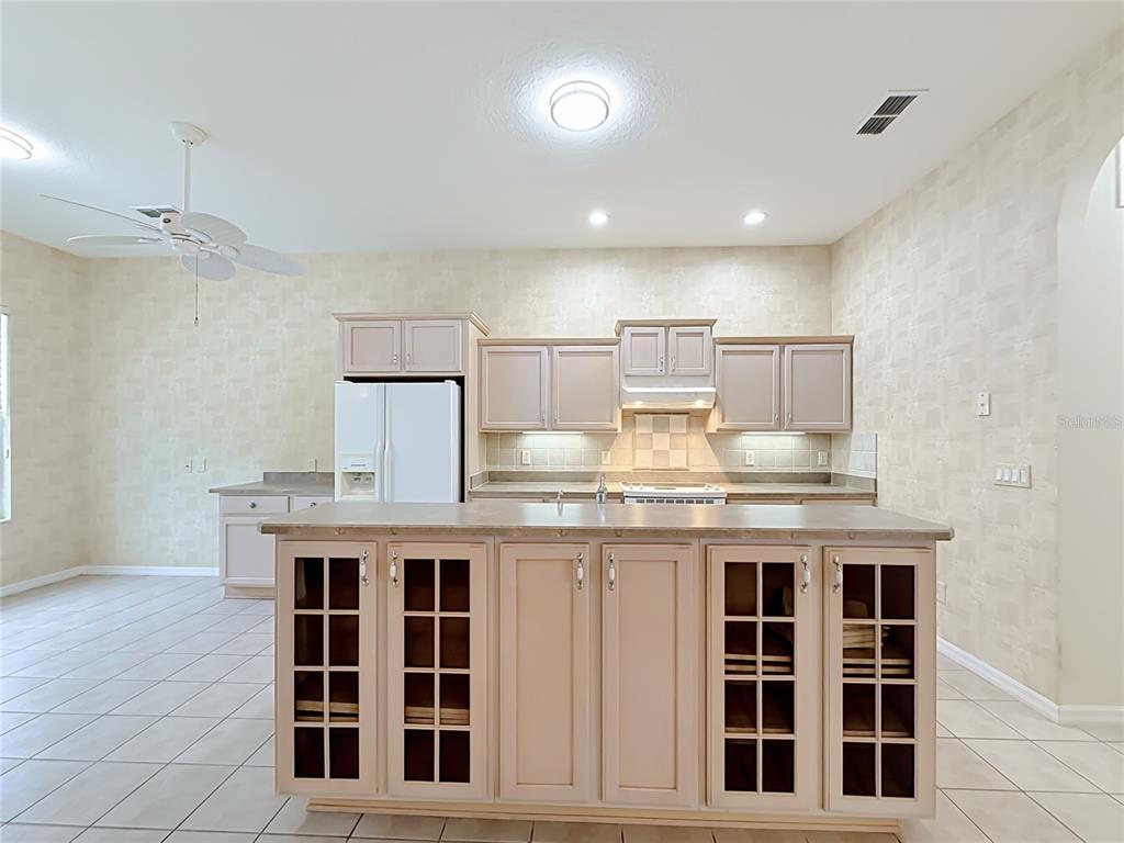 A kitchen features light-colored cabinets, a central island with glass-front doors, and tiled flooring — 11932 SE 179TH STREET, SUMMERFIELD, FL