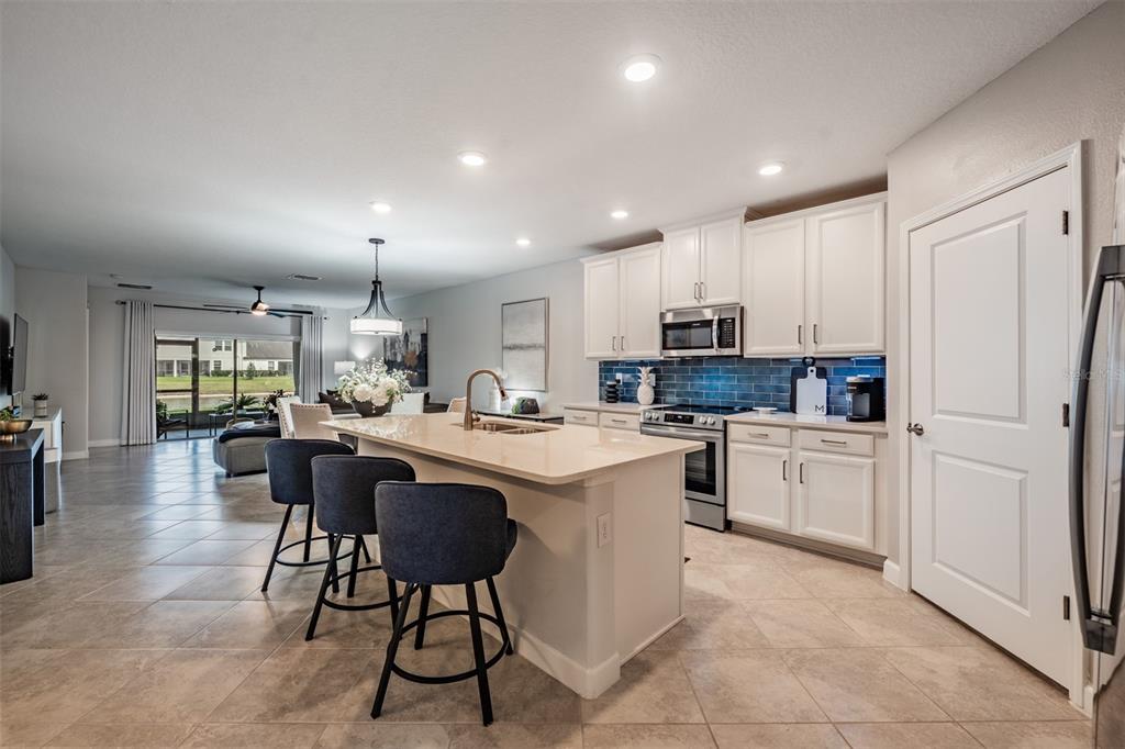A kitchen with white cabinets, a quartz-topped island, and blue tile backsplash opens to a living area — 10191 ECHO DOCK LOOP, SAN ANTONIO, FL