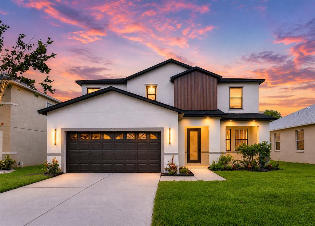 A two-story house with a white stucco exterior, a dark garage door, and a sunset sky — 1712 ATLANTIC DRIVE, RUSKIN, FL