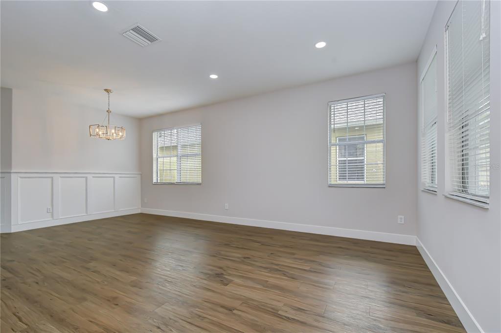 An empty room with wood-look flooring, white wainscoting, a chandelier, and multiple windows — 1712 ATLANTIC DRIVE, RUSKIN, FL