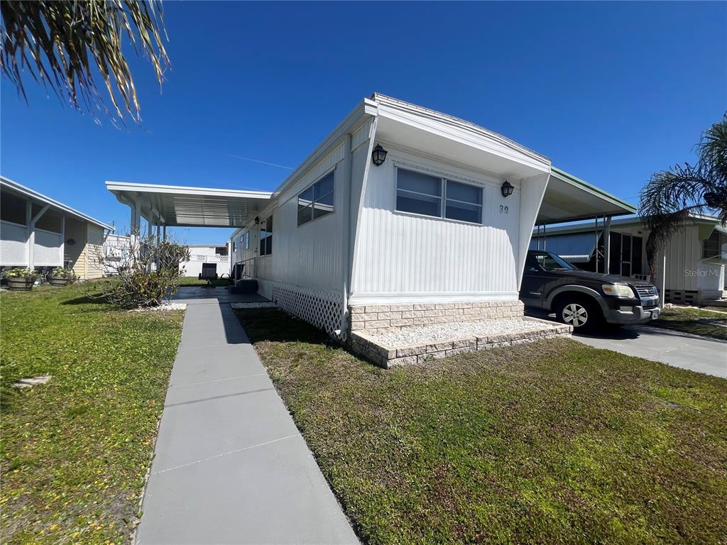 A white mobile home with a carport, a concrete walkway, and a brick-accented front entrance — 1500 COUNTY ROAD 1 UNIT 39, DUNEDIN, FL