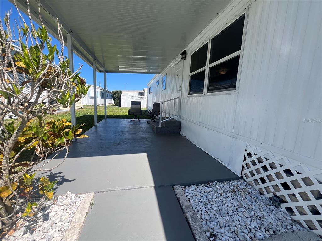 A covered concrete patio sits beside a white mobile home with lattice skirting — 1500 COUNTY ROAD 1 UNIT 39, DUNEDIN, FL