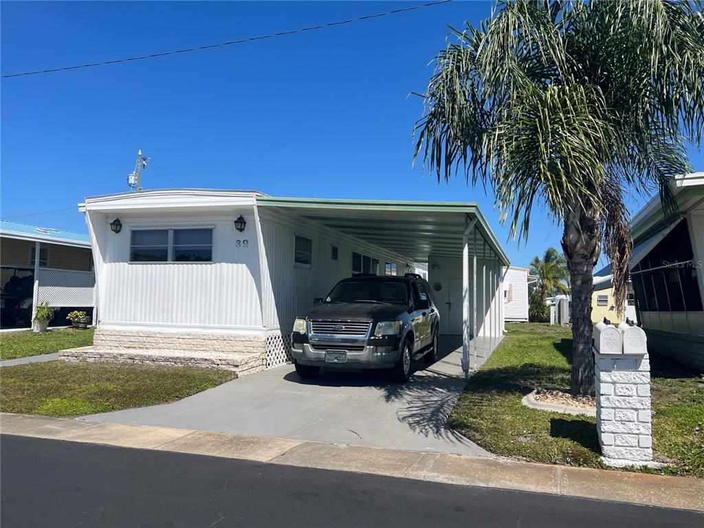 A single-story mobile home with a carport, a parked SUV, and a palm tree — 1500 COUNTY ROAD 1 UNIT 39, DUNEDIN, FL