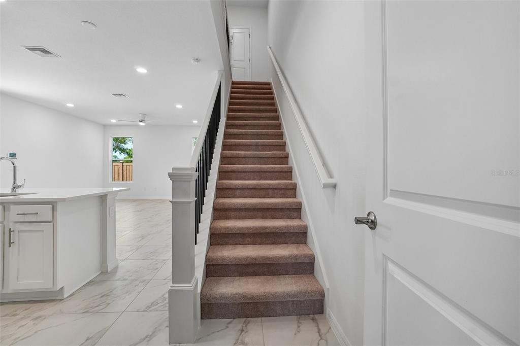 A staircase with brown carpet and a black railing leads upstairs next to a kitchen — 616 SILVER STREAM COURT, BRANDON, FL