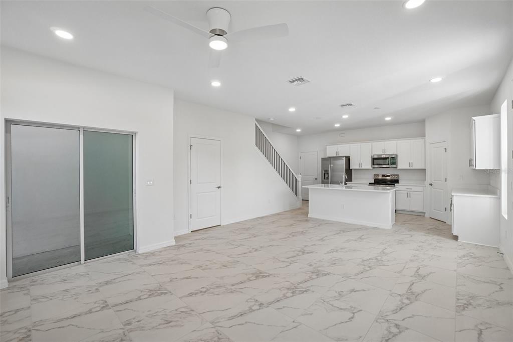 An open-concept kitchen and living area features white cabinetry, marble-look tile flooring, and a staircase — 616 SILVER STREAM COURT, BRANDON, FL