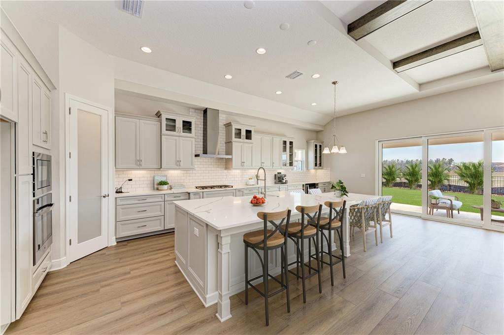 A modern kitchen features white cabinets, a large quartz island with stools, and sliding glass doors — 35576 BIG HAWK DRIVE, ZEPHYRHILLS, FL
