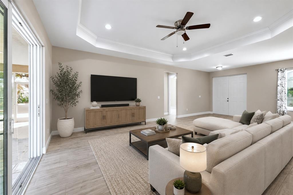 A living room features a tray ceiling, a large sectional sofa, and a media console — 3498 DUNKIRK STREET, PORT CHARLOTTE, FL