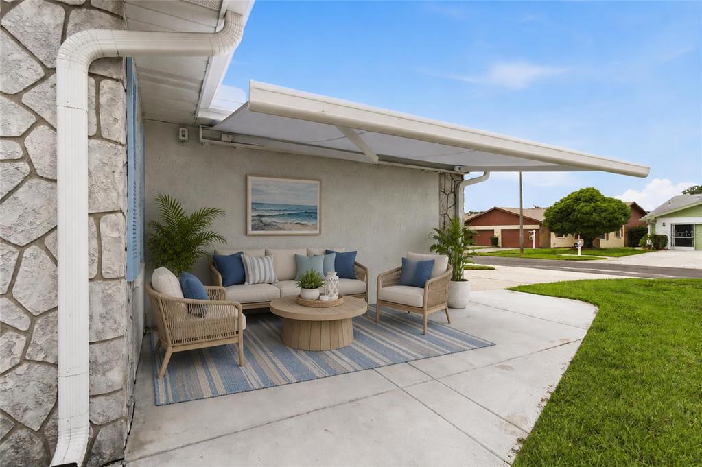 A patio features a retractable awning, outdoor furniture, and a striped rug on concrete — 3271 MCMATH DRIVE, PALM HARBOR, FL