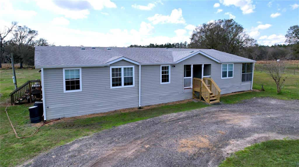 A light gray manufactured home with a gravel driveway and wooden stairs leading to entrances — 14890 CR 757, WEBSTER, FL