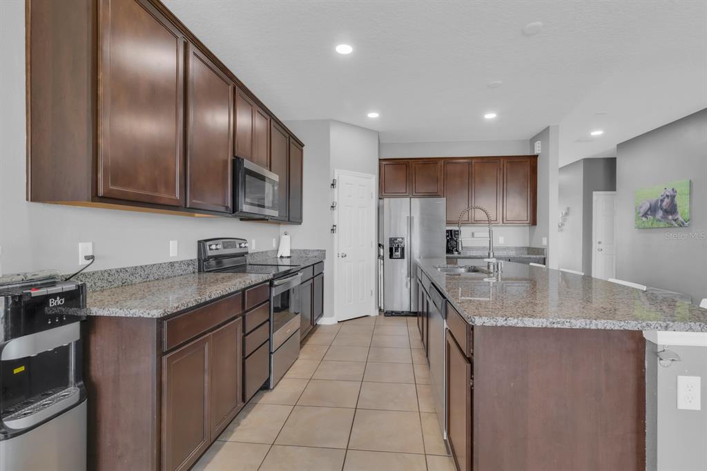 A kitchen features dark wood cabinets, granite countertops, stainless steel appliances, and tile flooring — 2172 BUR OAK BOULEVARD, ST CLOUD, FL