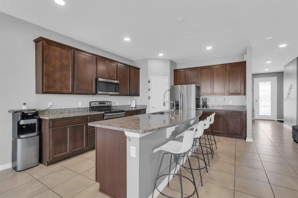 A kitchen features dark wood cabinets, granite countertops, a center island with bar stools, and tile flooring — 2172 BUR OAK BOULEVARD, ST CLOUD, FL