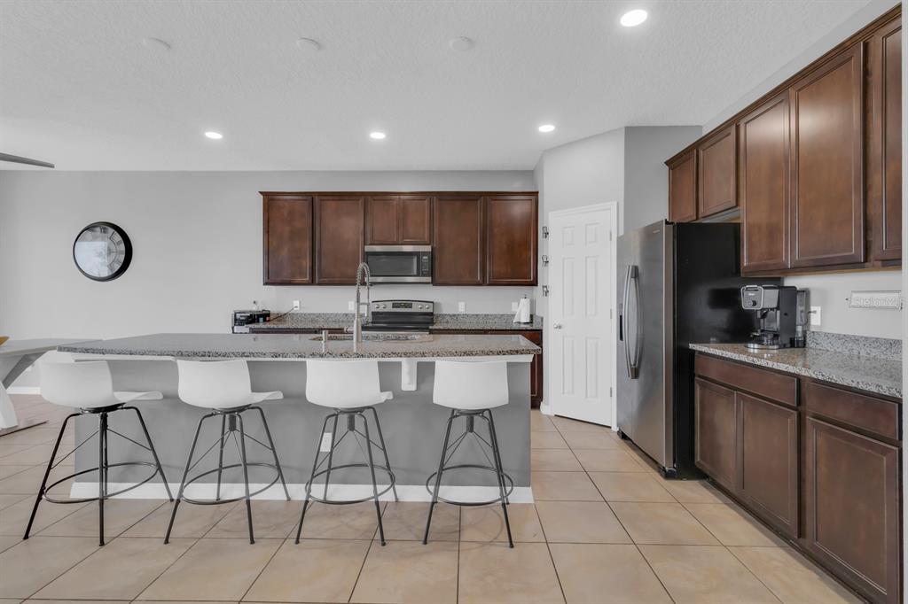 A kitchen features dark wood cabinets, granite countertops, a center island, and four white stools — 2172 BUR OAK BOULEVARD, ST CLOUD, FL