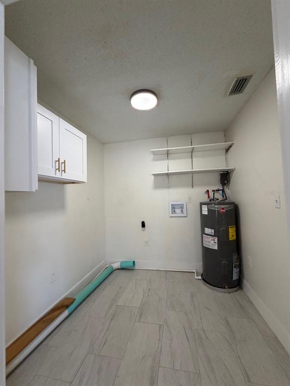 A laundry room features a water heater, wall-mounted shelving, white cabinets, and light-colored tile flooring — 2711 WILLOW RUN, ORLANDO, FL
