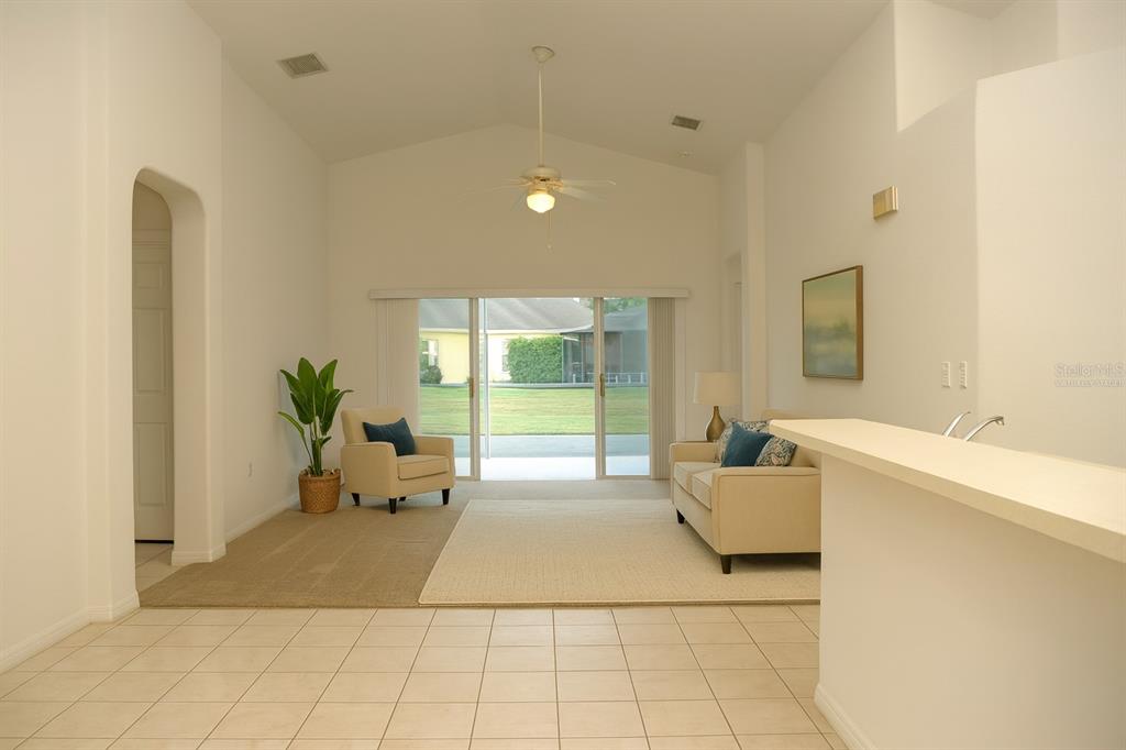 A living room with vaulted ceilings, tile flooring, a beige sofa, and sliding glass doors — 969 ANDALUSIA LOOP, DAVENPORT, FL