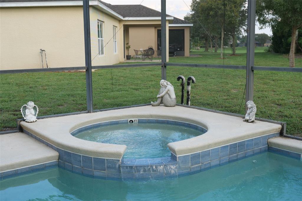 A raised spa with a spillover edge sits beside a swimming pool inside a screened enclosure — 969 ANDALUSIA LOOP, DAVENPORT, FL