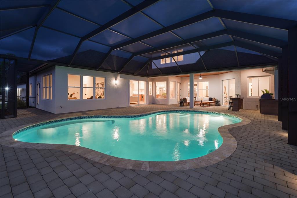 A swimming pool sits on a paved patio enclosed by a large screened lanai structure — 7310 201ST STREET E, BRADENTON, FL