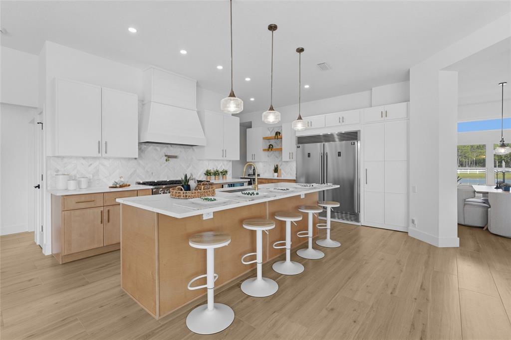 A modern kitchen features a large island with bar stools, white cabinetry, and wood flooring — 7310 201ST STREET E, BRADENTON, FL