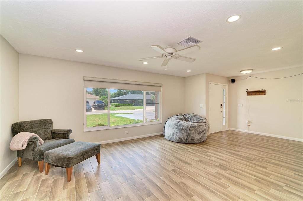 A living room features light wood-look tile flooring, a large window, a ceiling fan, and furniture — 2011 37TH STREET W, BRADENTON, FL