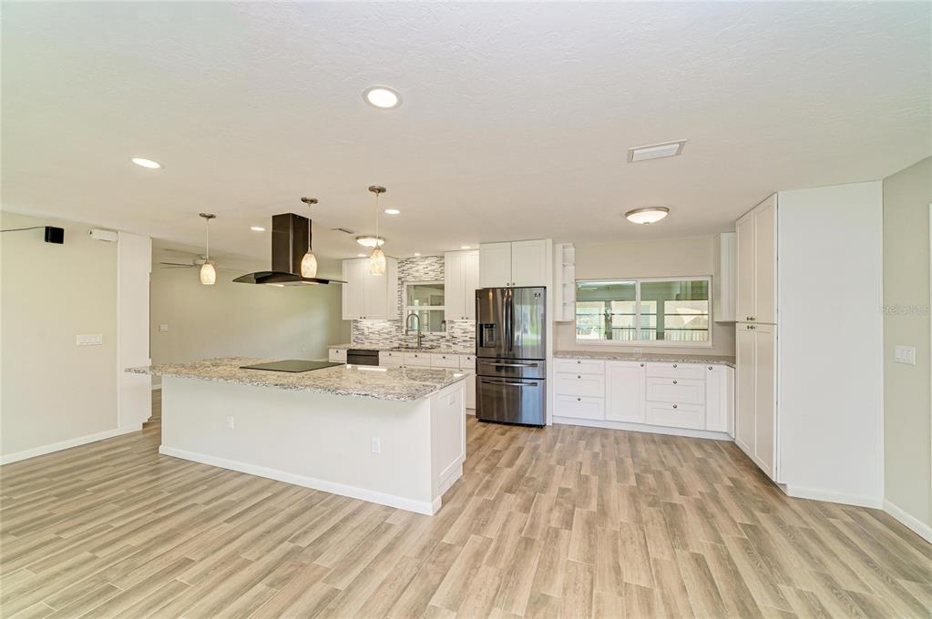 A modern kitchen features white cabinetry, granite countertops, a center island, and wood-look tile flooring — 2011 37TH STREET W, BRADENTON, FL