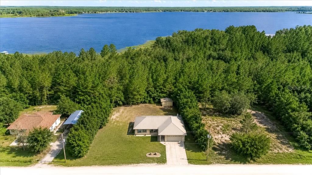 An aerial view shows a house with a metal roof situated on a wooded lakefront lot — 21875 NE 135TH LANE, FORT MC COY, FL