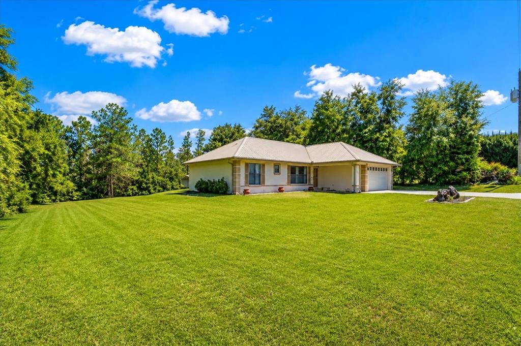 A single-story house with a light-colored exterior and a metal roof sits on a lawn — 21875 NE 135TH LANE, FORT MC COY, FL