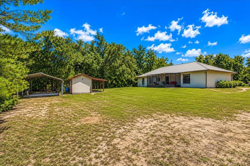 A backyard view showing a house with a screened porch, a shed, and a carport — 21875 NE 135TH LANE, FORT MC COY, FL