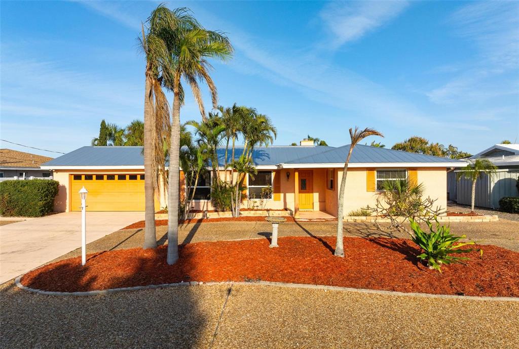 A single-story house with a blue metal roof, orange garage door, and palm trees — 5207 BIMINI DRIVE, BRADENTON, FL