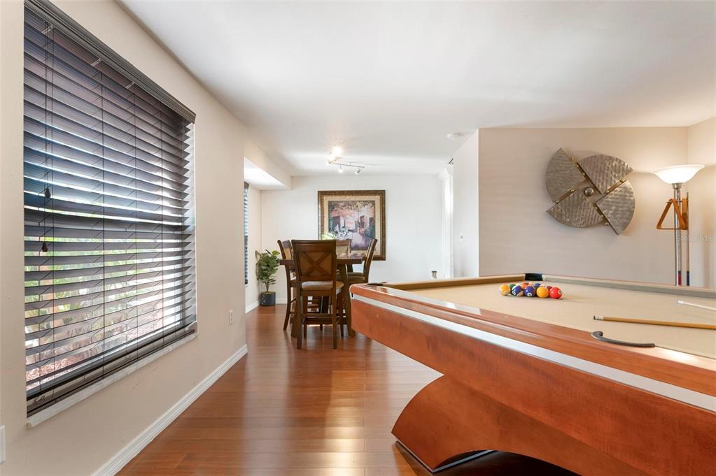 A room with hardwood floors features a pool table in the foreground and a dining set — 5207 BIMINI DRIVE, BRADENTON, FL