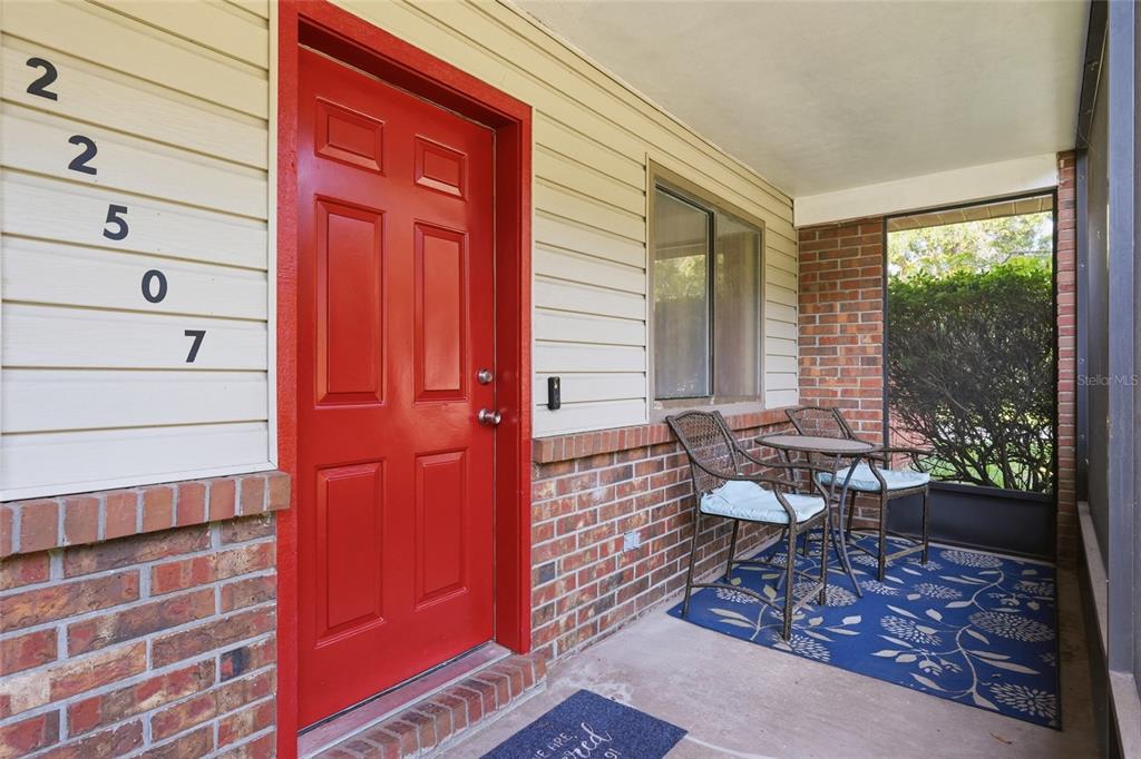 A red front door sits next to a small patio with two chairs and a rug — 22507 NW 176TH PLACE, HIGH SPRINGS, FL
