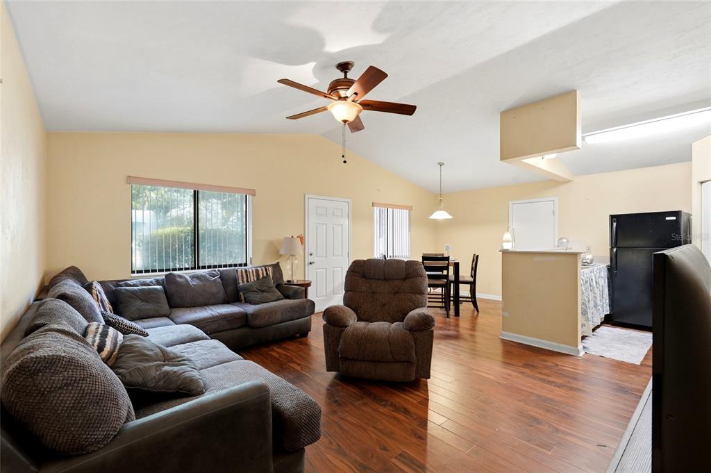 A living room with wood flooring, a vaulted ceiling, a ceiling fan, and an open kitchen — 22507 NW 176TH PLACE, HIGH SPRINGS, FL