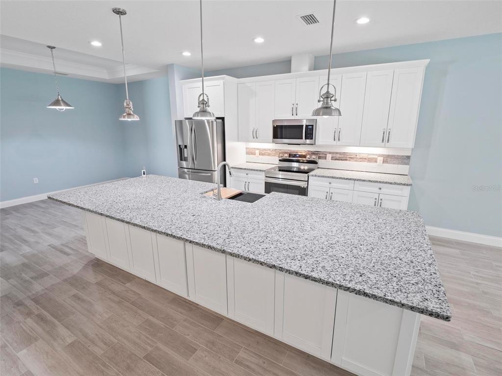 A kitchen features a large granite-topped island, white cabinetry, and stainless steel appliances — 127 ULLIAN TRAIL UNIT B, PALM COAST, FL