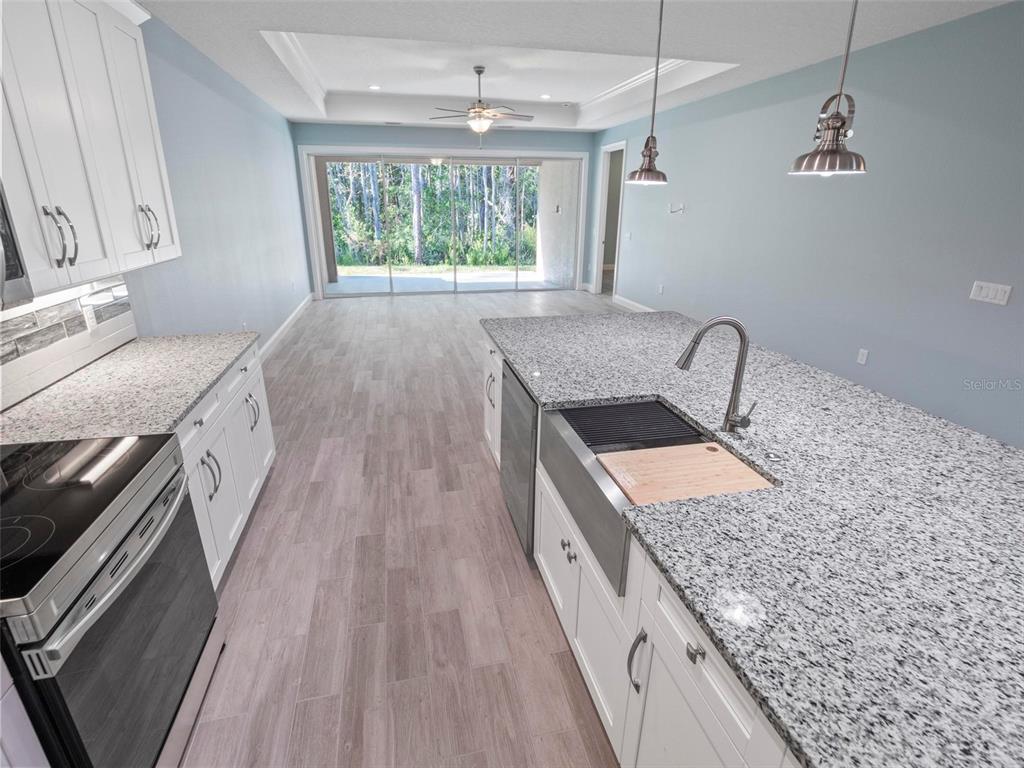 A kitchen with white cabinets, granite countertops, a farmhouse sink, and light wood-look flooring — 127 ULLIAN TRAIL UNIT B, PALM COAST, FL
