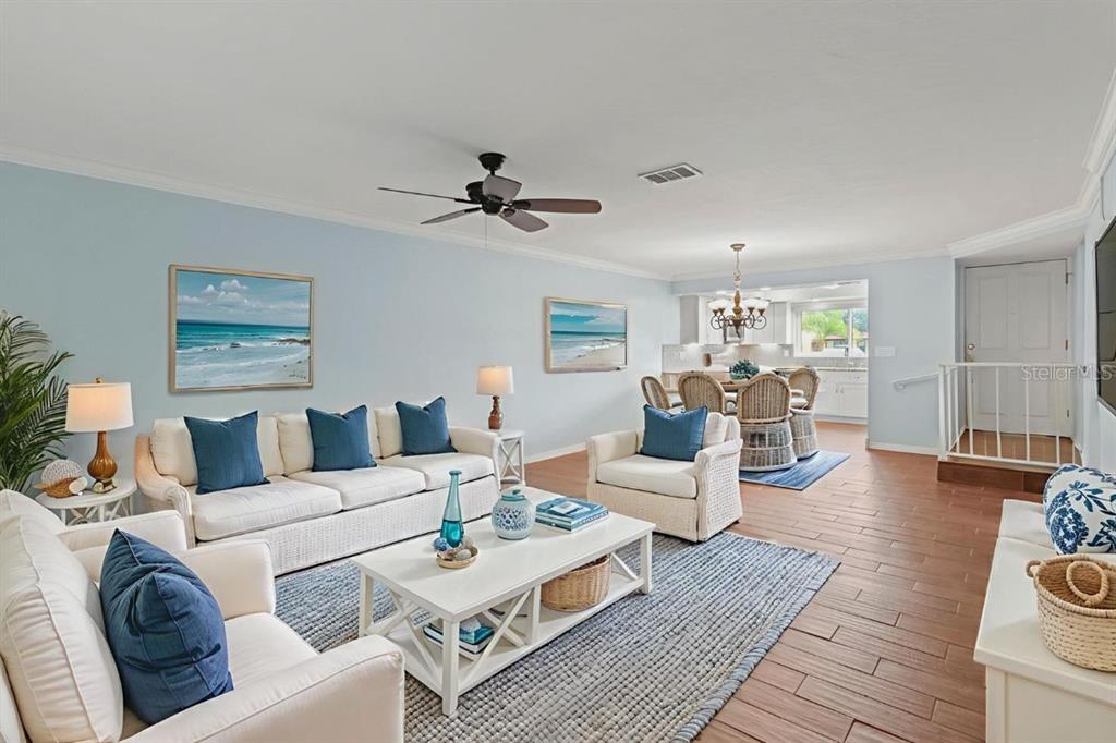 A bright living room features white furniture, blue accents, and wood-look tile flooring — 1446 56TH STREET W UNIT #1446, BRADENTON, FL