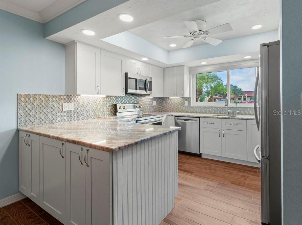 A kitchen with white cabinets, a stone countertop, a tiled backsplash, and stainless steel appliances — 1446 56TH STREET W UNIT #1446, BRADENTON, FL
